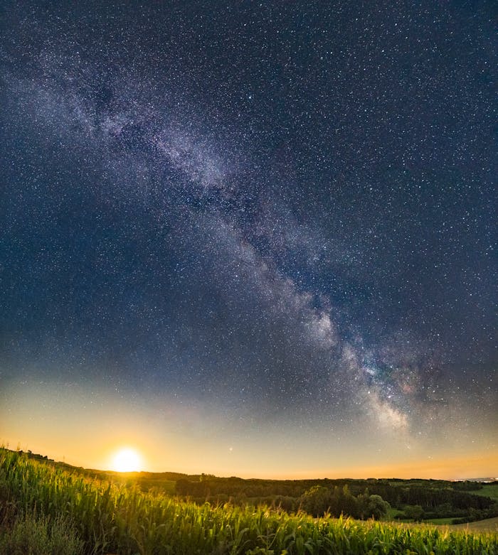 Captivating view of the Milky Way galaxy with a sunset over a serene green field.